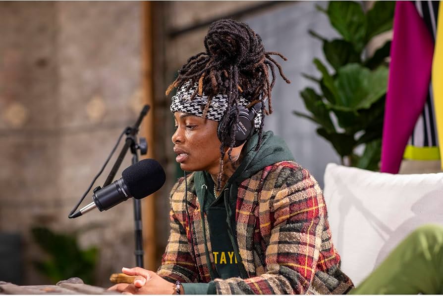Two microphones on stands in front of lounge chairs on a small stage set up for a podcast recording in an intimate venue