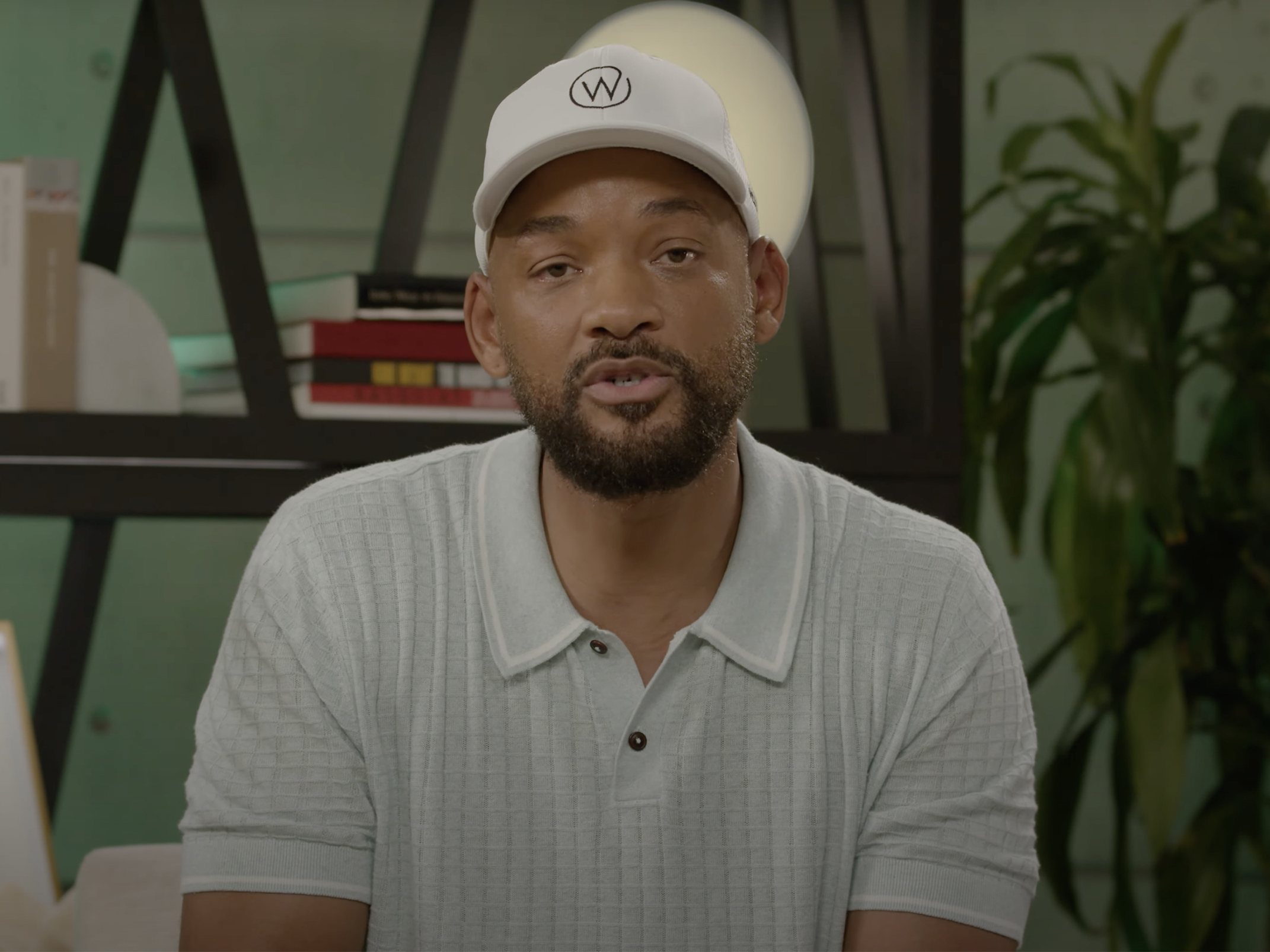 Will Smith sits indoors and addresses the camera in a formal apology video frame.